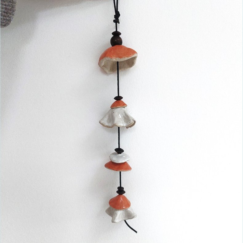 Vindklokke i orange og sandfarvet glasur. Har sort l�dersnor og m�rke tr�perler. 